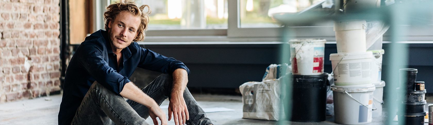 A man is sitting on the floor of an empty apartment and is looking pensively. 