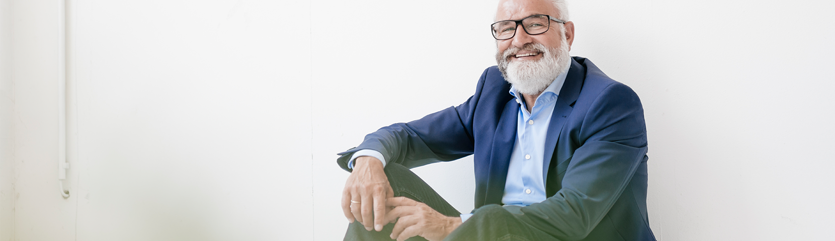 A man at the retirement age is sitting on the floor of room and smiles at the camera. 