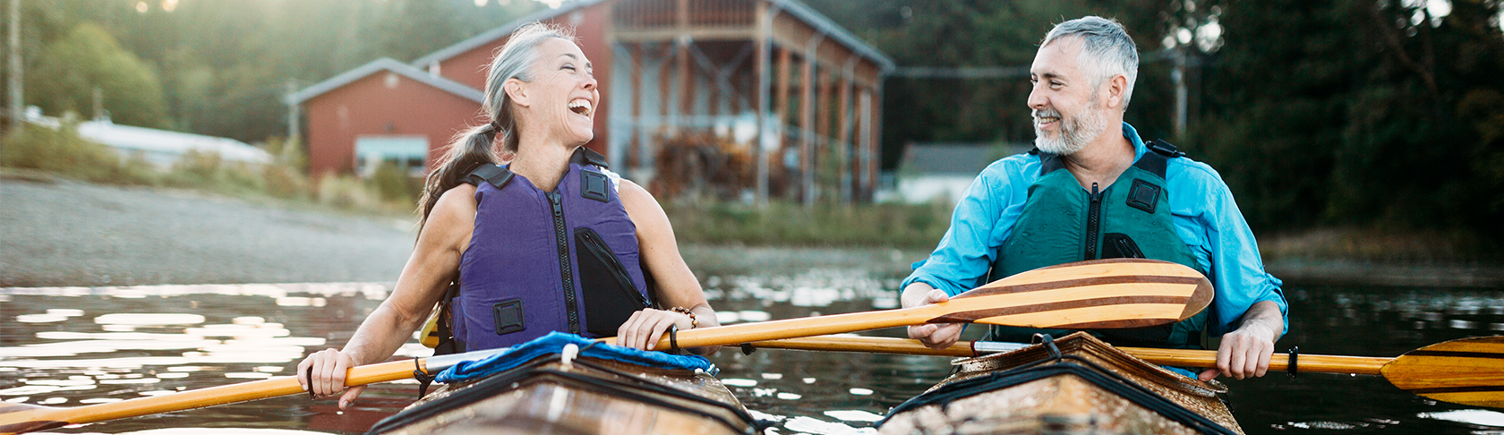 Un couple en âge d’être retraité est assis dans deux kayaks et se sourit.