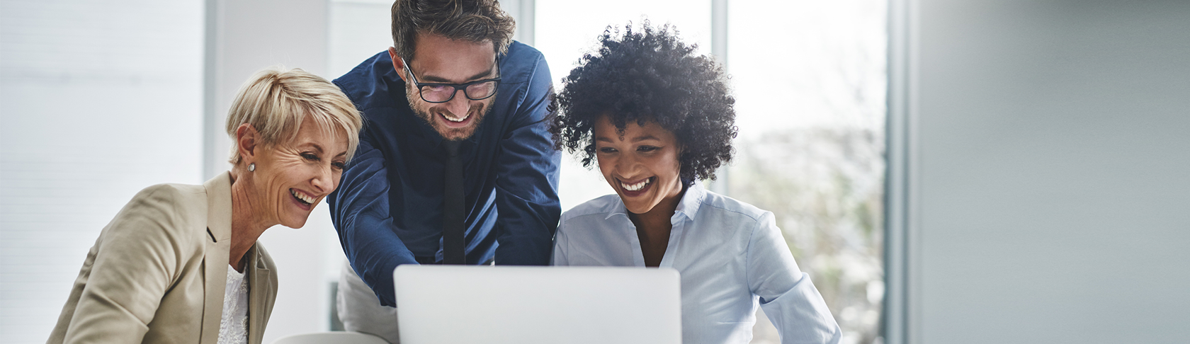 Zwei Frauen und ein Man sitzen an einem Sitzungstisch und schauen gemeinsam auf einen Laptop-Bildschirm. 